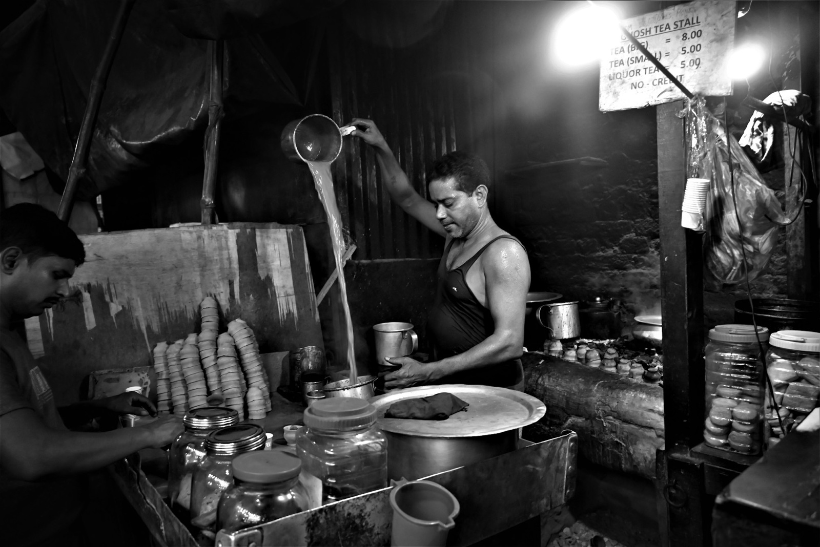 A chai wala pouring tea from a height at a roadside stall in India