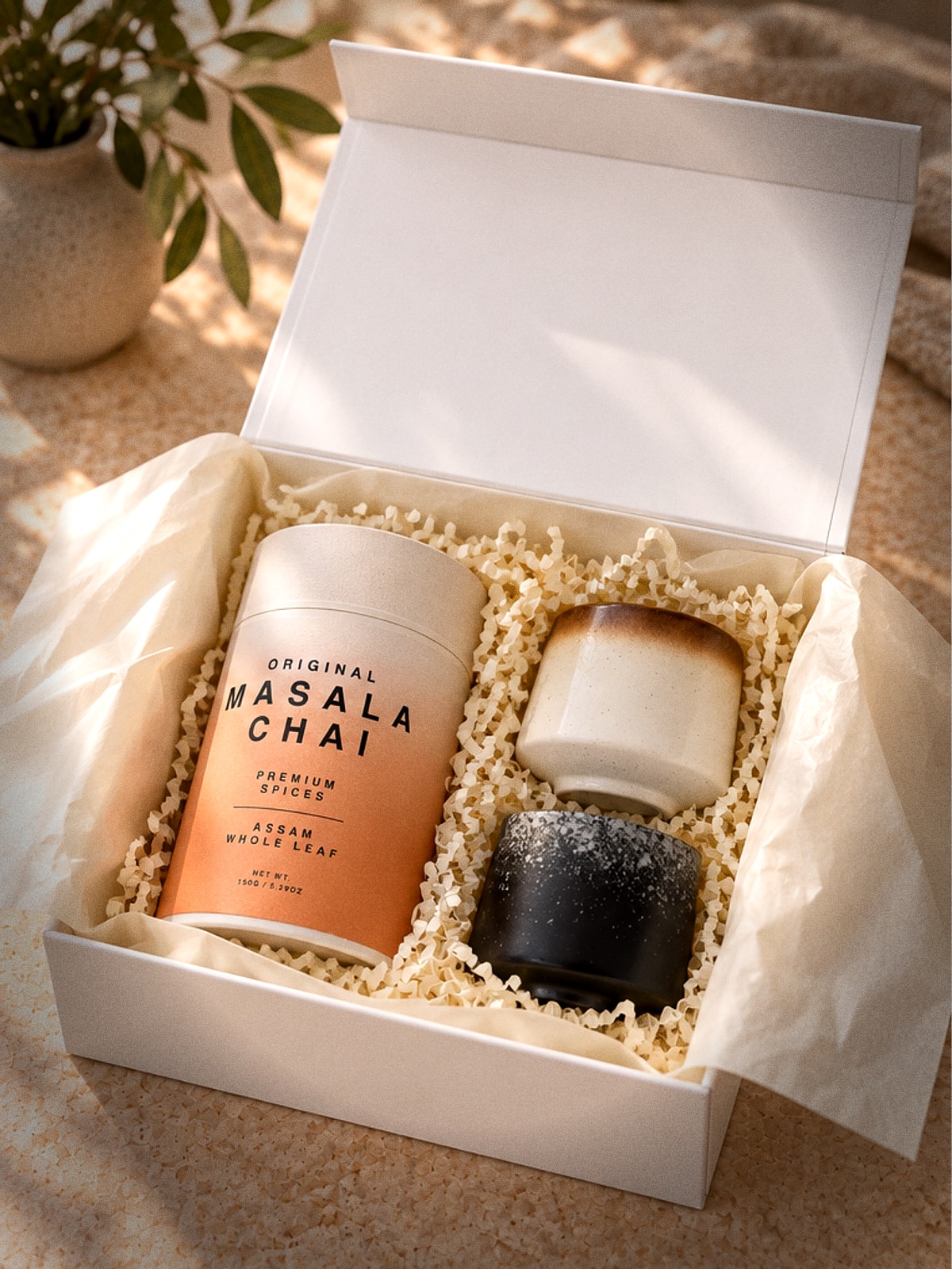 The gift box open, ivory tissue folded back over crinkle paper holding the chai tube and two cups